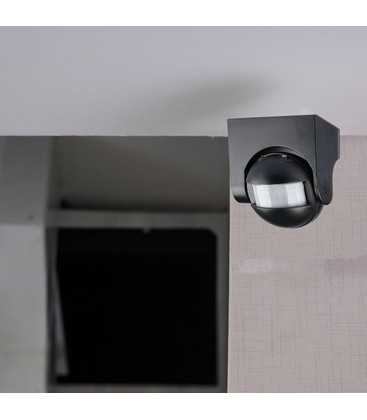 Svart rörelsesensor monterad på vägg i en utomhusmiljö som visar fast installation.